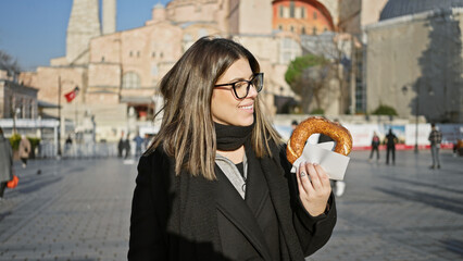 Obraz premium Smiling woman holding a simit in istanbul with historic hagia sophia in the background on a sunny day.