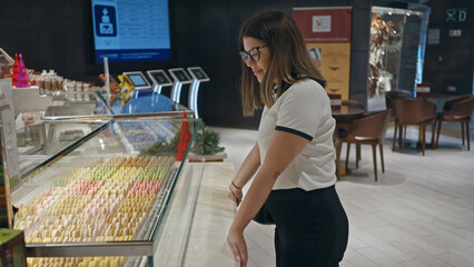A young woman peruses colorful macarons at a modern pastry shop.
