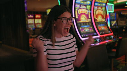 Excited young woman celebrating a win at slot machines in a casino.