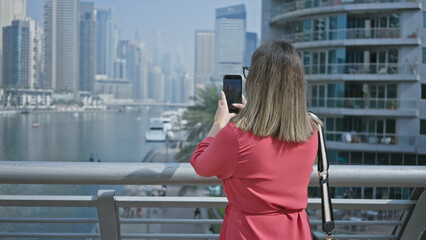 Brunette woman photographing dubai skyline with smartphone, showcasing city, marina, and luxury.