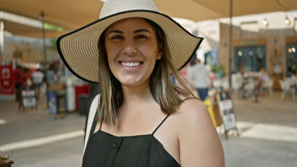 A smiling young woman wearing a sunhat poses in a bustling dubai souk market