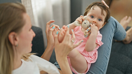 Mother and daughter sitting on sofa playing together holding feet at home