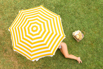Woman in a white bikini with basket for picnic sitting on deck chair under yellow umbrella  on the...