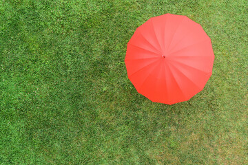 Red umbrella on the green grass sunbathes at summer day. Top view, drone, aerial view.