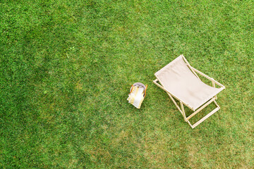 Deck chair, basket for picnic, headphones on the green grass at summer day. Top view, drone, aerial view.