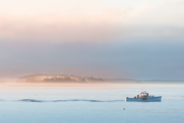 Lobster boat setting traps at sunrise along the coast of Maine. Fog covered islands in distance...