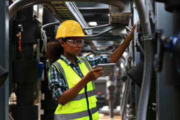 Female engineer wearing a yellow safety vest and yellow helmet  working check Industry cooling system, HVAC of large industrial building 