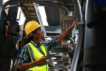 Female engineer wearing a yellow safety vest and yellow helmet  working check Industry cooling system, HVAC of large industrial building  - obrazy, fototapety, plakaty
