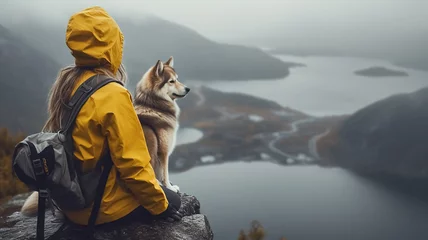 Foto op Canvas Cinematic image of a hiker girl sitting with husky at the top of the mountain with rocks, autumn trees and lake. Long shot of a beautiful scene in autumn from the top. Moody colors. © Loucine