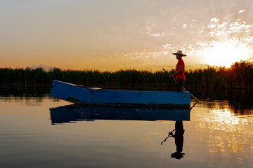 Fototapeta na wymiar Local fisherman rowing a boat on a river in the early morning hours. person in small wooden boat on calm sea at sunrise