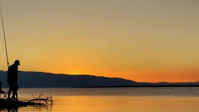 Fishermen at sunset of Issyk-Kul mountain lake, Kyrgyzstan. The sun goes behind the mountains at sunset. Calm, peaceful natural background. Lake with a view of the Tien Shan Mountains. Kyrgyzstan 4K