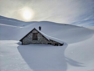 Freeriders ride over a snow covered house roof. Skiers go up to the roof of an alpine hut and back...