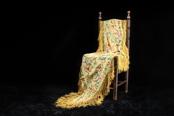 SPANISH STILL LIFE OF FLAMENCO DANCE WITH MANILA SHAWL ON A SEVILLE TYPICAL CHAIR. BLACK BACKGROUND.