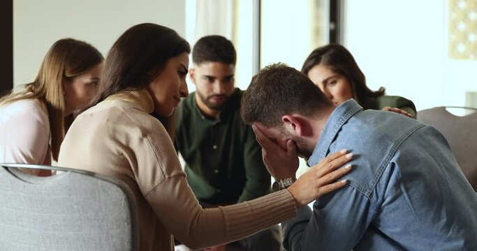 Young upset man receive psychological support from therapy counseling team mates, group of people listen life concerns empathize, comforting, express care to stressed, unhappy session member. Therapy