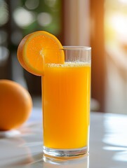 Fresh orange juice in tall clear glass with slice of orange on rim, set on white table with blurred background