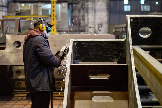 Worker in a mask grinds a metal part at a factory or cuts it with an electric circular saw