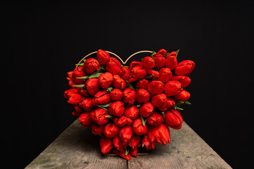 red tulips tied as heart shape on table with black background and space for text