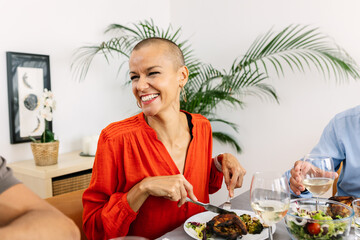 Happy mid adult woman enjoying dinner with her family at home. Group of people celebrating together...