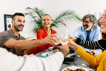 Happy group of multi-generational family gathered at dinner table toasting wine celebrating...