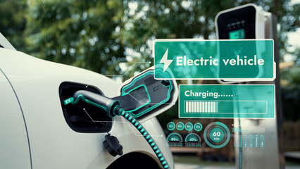 Electric car plug into EV charger cable from charging station display smart digital battery status hologram in eco green park and foliage background. Energy sustainability technological advance.Peruse