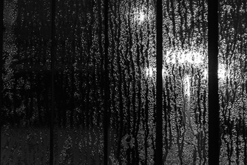 Light through raindrops on glass, abstract street background in bokeh, monochrome, black and white