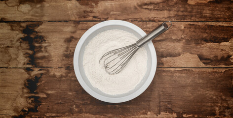 Flour and whisk in a mixing bowl on rustic wood