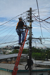 Unidentifiable electrician climbing a power pole to repair the tangled cables. Power line installer with inadequate work protection such as a hard hat. Manaus, Amazonas state, Brazil.