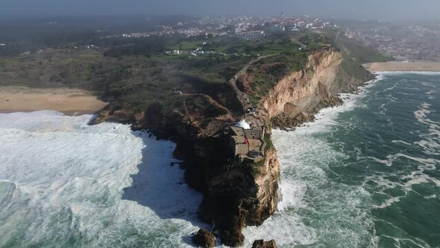 Aerial view. A red lighthouse on a huge cliff. Nazaré city, Portugal. The ocean in soft sunset rays.  4k stock video