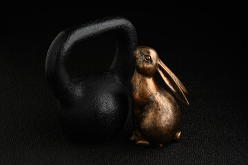 Holiday fitness and Happy Easter, gold metal bunny with a black iron kettlebell on a black...
