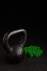 Holiday fitness and Happy St. Patick’s Day, green glitter shamrock shape with a black iron kettlebell on a black background
