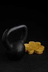 Holiday fitness and Happy St. Patick’s Day, gold glitter shamrock shape with a black iron kettlebell on a black background
