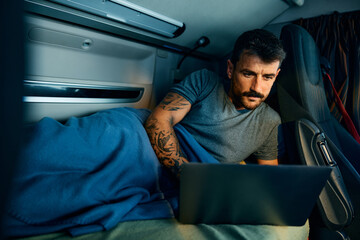 Truck driver using laptop while resting in vehicle cabin at night.