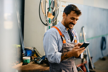Happy mechanic using smart phone while working in repair shop.