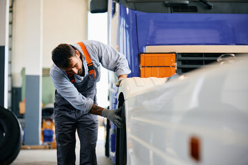 Truck mechanic inspecting tires of vehicle in garage.