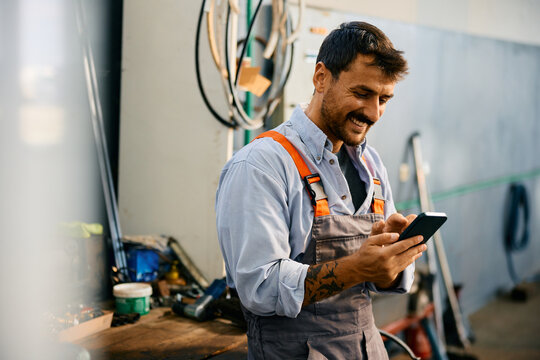 Happy mechanic using smart phone while working in repair shop. - Powered by Adobe
