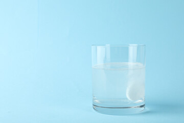 Glass of water with effervescent tablet on light blue background, space for text