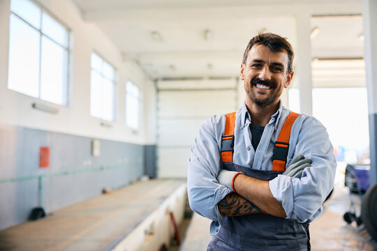 Happy mechanic with arms crossed at truck repair workshop looking at camera.