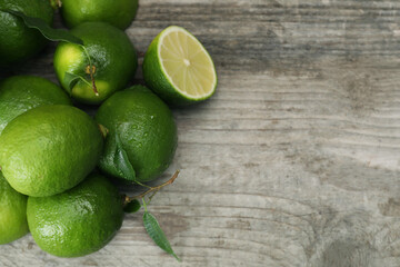 Pile of fresh wet limes and leaves on wooden table, top view. Space for text