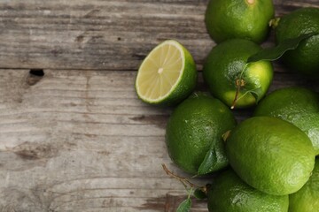 Pile of fresh wet limes and leaves on wooden table, top view. Space for text