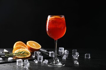 Glass of tasty Aperol spritz cocktail with orange slices and ice cubes on table against black...