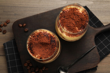 Delicious tiramisu in glasses, spoon and coffee beans on wooden table, top view