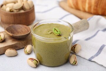 Tasty pistachio cream and nuts on light table, closeup