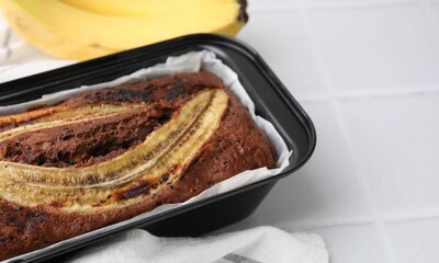 Delicious banana bread and fresh fruits on white tiled table, closeup. Space for text