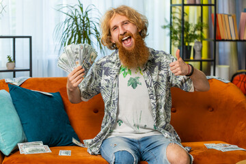 Successful happy rich Caucasian redhead man counting money cheering up with high profits, lottery...