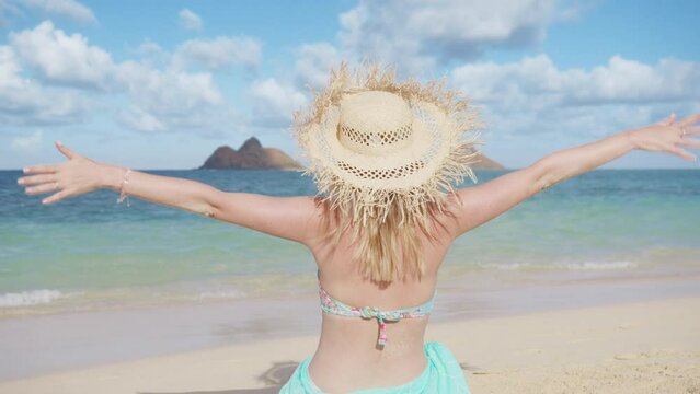 Back view of traveler showing friendly shaka hawaiian sign both hands. Tourist woman in wide straw fringed hat relaxing on summer vacation. Happy female in bikini on Hawaii island. Girl enjoying beach
