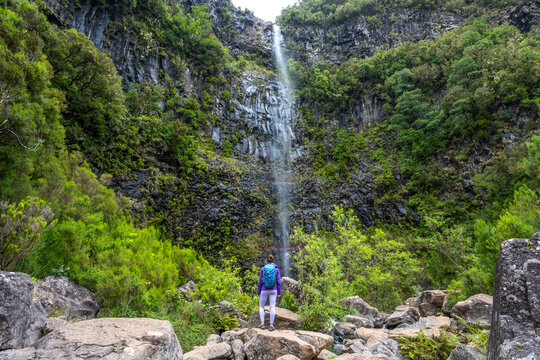 Female tourist with backpack enjoys atmosphere at waterfall falling from high rock wall. Lagoa do Vento waterfall, Madeira Island, Portugal, Europe.