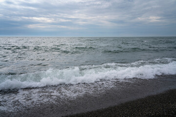 An incoming wave on the Black Sea and a pebble beach on the Sochi coast on a summer day with clouds, Sochi, Krasnodar Territory, Russia