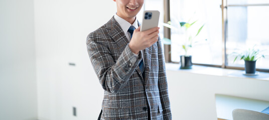 オフィスで携帯を持ち考える若手のビジネスマン
