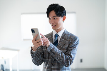 オフィスで携帯を持ち考える若手のビジネスマン
