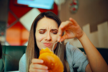 Woman Finding a Nasty Ingredient in a Fast-Food Sandwich. Unhappy customer examining the restaurant...